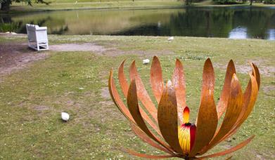 A large flower sculpture with lake and amphitheatre in the background