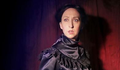 Startled woman looking at camera, in highneck black silk Victorian dress.