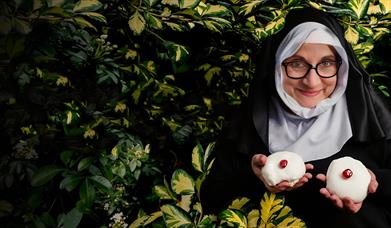 Woman dressed as nun, holding up two chelsea buns.
