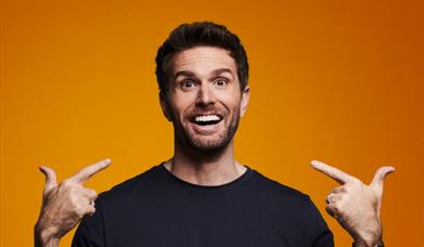Joel Dommett smiling and pointing at himself