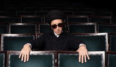 John Cooper Clark sat in dark auditiorium.