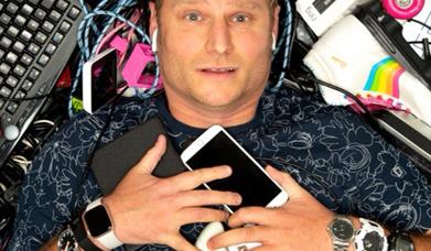 Scott lying on his back in a pile of phones, remote controls, roller skates, dolls, keyboards etc.